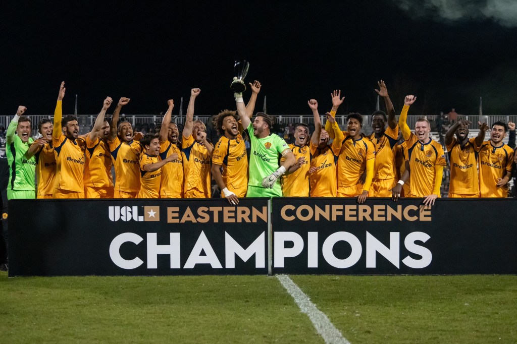 Rhode Island FC players celebrate on the field in front of cheering fans at Beirne Stadium, capturing the energy and unity of game day. The image comes from winning the USL Championship Eastern conference
